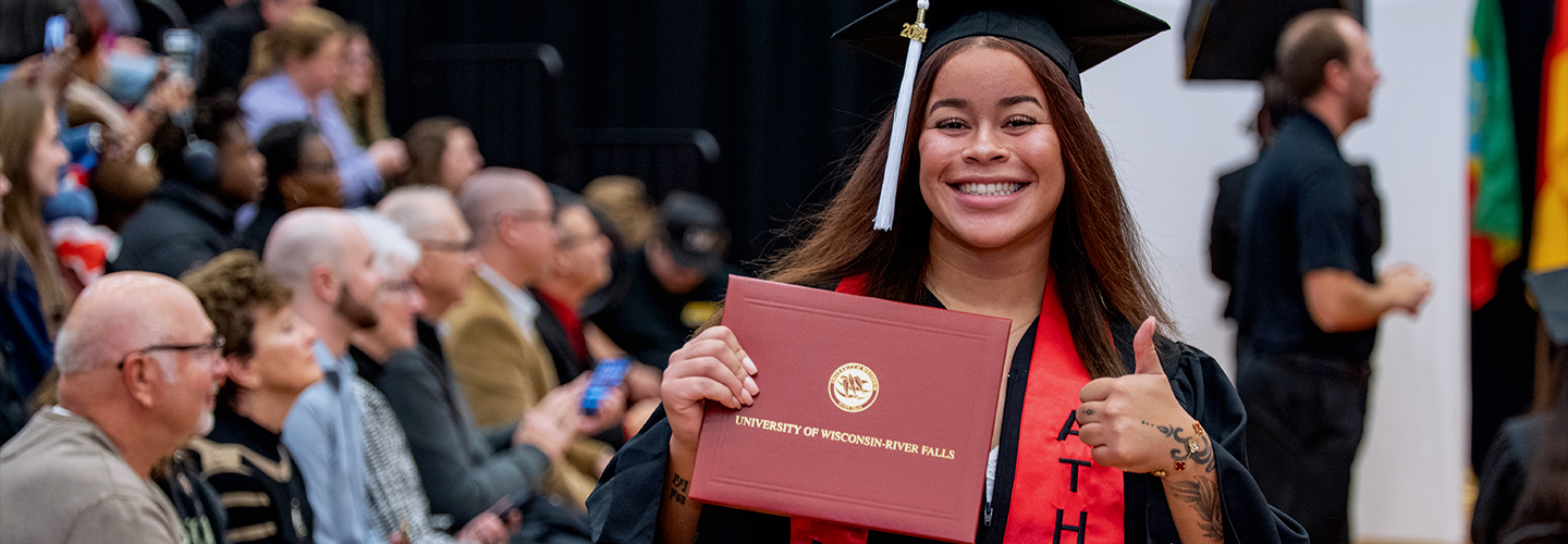 A undergraduate student smiles for the camera and holds up her degree after walking across the stage at the commencement ceremony