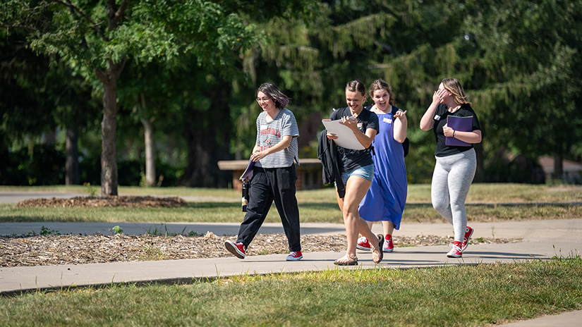 students laugh as they walk across a campus sidewalk