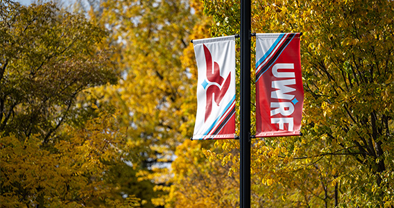 A banner displays the UWRF brand on a light post with the fall leaves behind it.