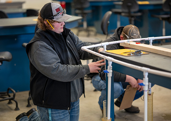 A student measures the length of PVC pipe during a building demonstration