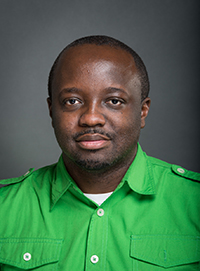 Hiawatha Smith headshot. A black man smiles at the camera while wearing a bright green button up shirt. He has short black hair and black facial hair and is posed in front of a grey backdrop.