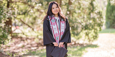 girl in graduation robe standing outside by trees