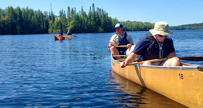 Two male students sit in a canoe and two other students are behind them in the background