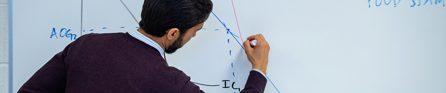 A professor writes a math equation on a whiteboard.