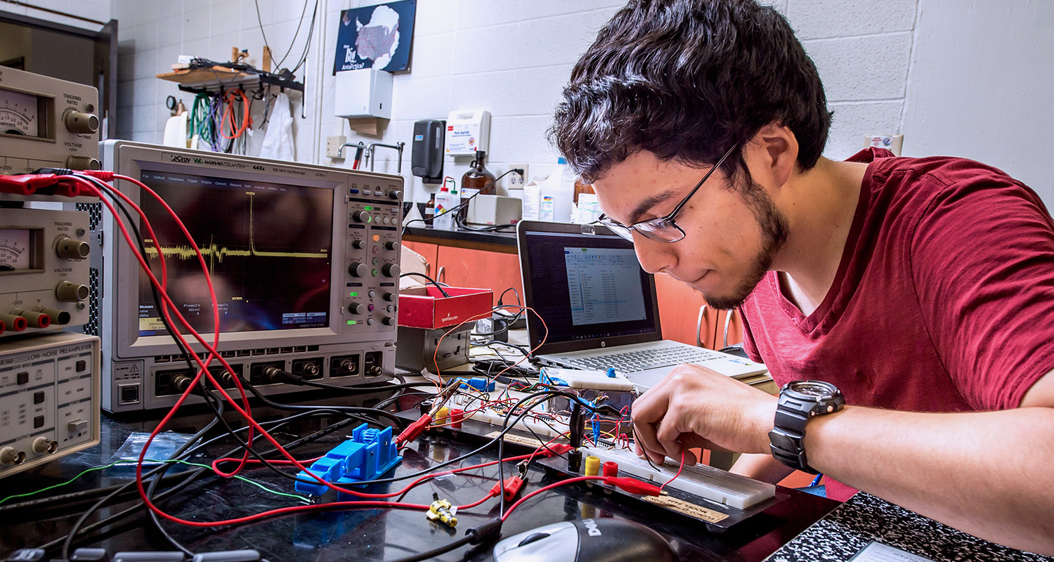 A male student places wires into a circuit board while doing an electricity experiment.