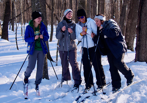 Four students pose while cross country skiing in a forest