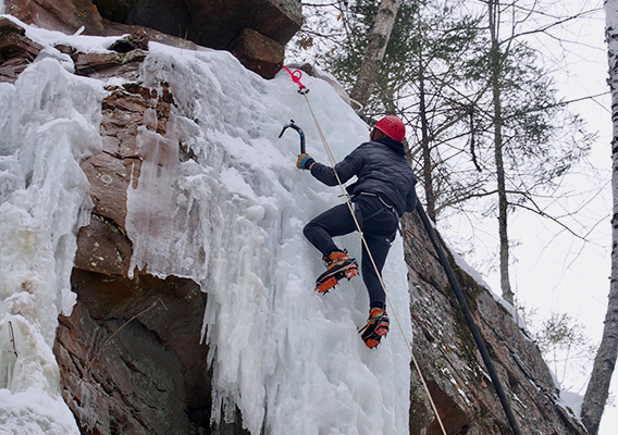 A student uses ice picks to climb up a frozen waterfall